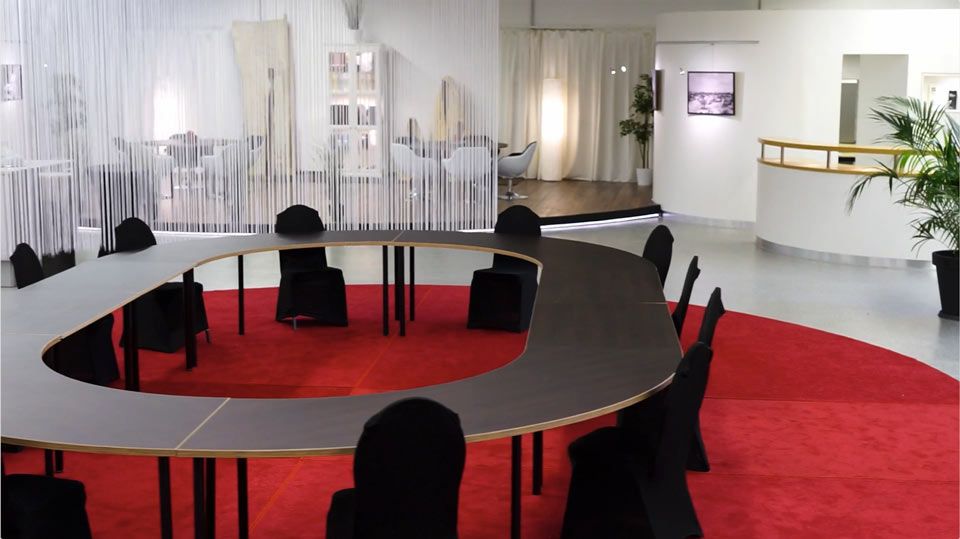 Moderner Konferenztisch mit runder Anordnung schwarzer Stühle auf rotem Teppich.
